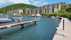 A marina with boats docked, a wooden dock, and a building with multiple balconies in the background. - Sapphire Dominica-Gorgeous View Walk to beach (St Thomas)
