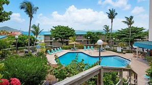 A pool area with lounge chairs, a wooden deck, and a view of a building with a blue roof. - Sapphire Dominica-Gorgeous View Walk to beach (St Thomas)