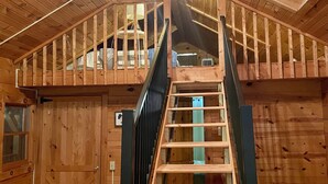 Un interior de madera con una escalera central, paredes de madera y un ventilador de techo.