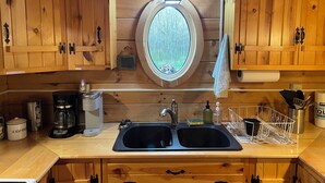 Una cocina con armarios de madera, un ventanal redondo, una cafetera y un lavamanos.