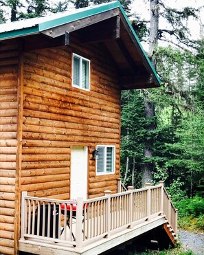 Une cabane en bois dotée d’un porche et d’une porte, entourée de forêt.