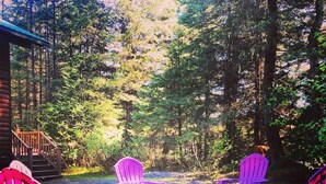 Uma cabana de madeira com varanda e área de fogueira com cadeiras Adirondack.
