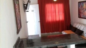 A small room with a bed, a desk, and a red curtain. - COMFORT DEPARTMENT (Puerto Vallarta)