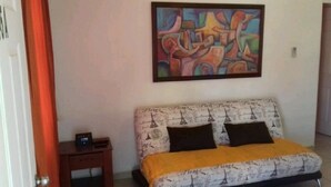 A bedroom with a bed, a nightstand, a painting, and a door. - COMFORT DEPARTMENT (Puerto Vallarta)