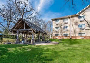 A lodge with a wooden pavilion, a grassy lawn, and a multi-story building in the background. - MainStay Suites Columbus near Fort Benning (Columbus)