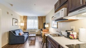A compact hotel room with a kitchenette, a sofa, a dining table, and a window with curtains. - MainStay Suites Columbus near Fort Benning (Columbus)