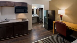 A compact kitchen with dark cabinets, a microwave, a refrigerator, and a small desk with a chair.