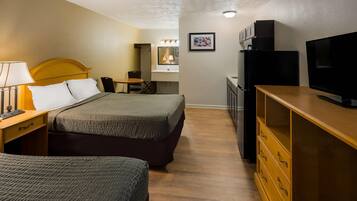 A hotel room with a bed, bedside table with lamp, dresser, TV, and a small desk with chair.