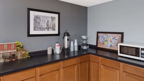 A kitchen with wooden cabinets, a black countertop, a coffee maker, a water dispenser, and a framed map.