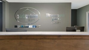 A reception desk with a grey wall behind it displaying the names 'Sunlight Extended Stay Hotel' and 'Rodeway Inn' along with the 'By Choice Hotels' logo. - Suburban Studios Brazil (Brazil)