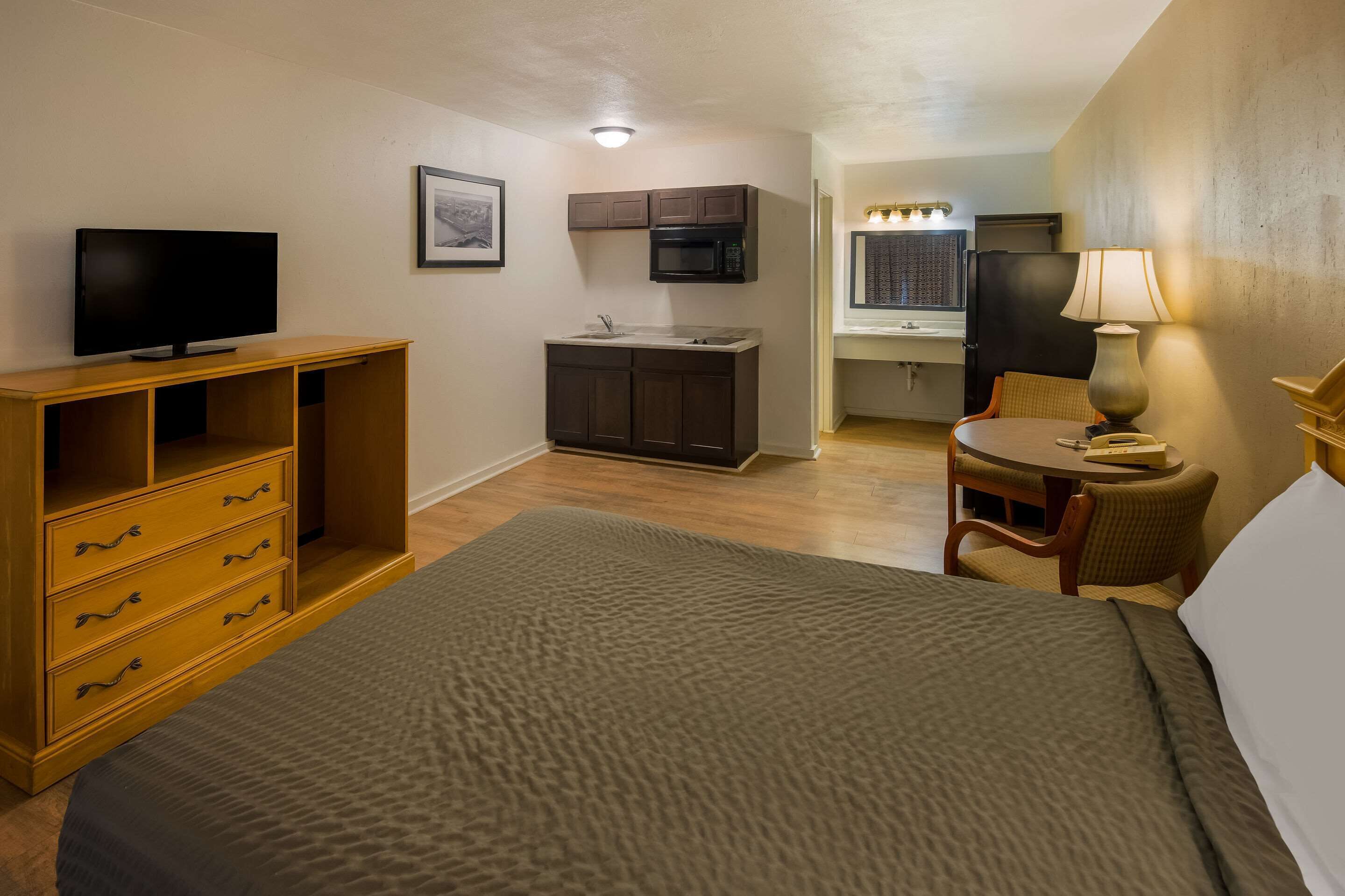 Ein kompaktes Hotelzimmer mit Bett, Fernseher, Küchenzeile und einer kleinen Essecke.
