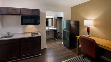 A compact kitchen with dark wood cabinets, a stainless steel refrigerator, a microwave, and a sink.