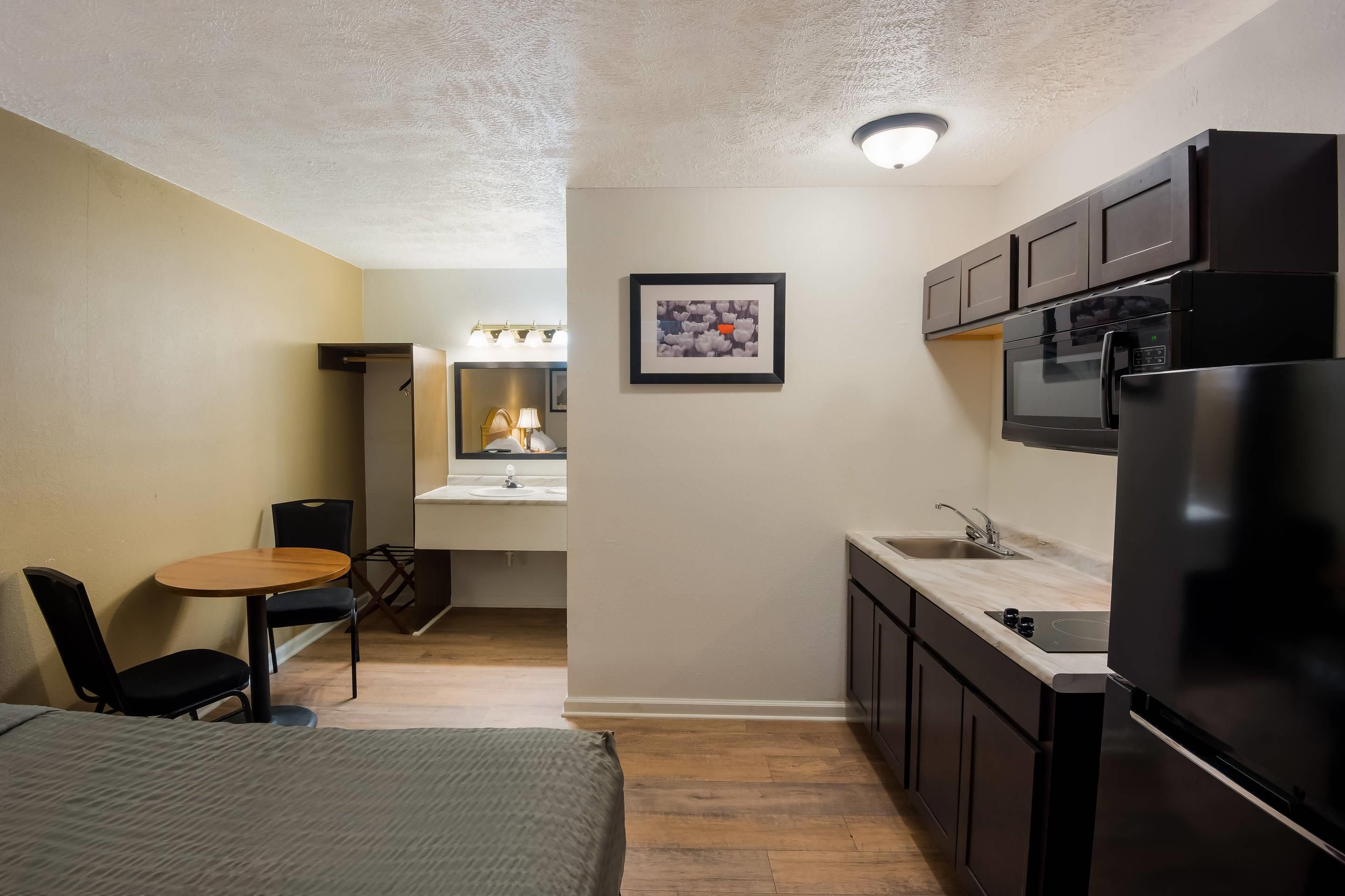 Une chambre d’hôtel compacte comprenant un lit, une petite table à manger avec des chaises, une kitchenette équipée d’un réfrigérateur, d’un four à micro-ondes et d’un évier, ainsi qu’une salle de bain avec douche et toilettes.