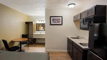 Une chambre d’hôtel compacte comprenant un lit, une petite table à manger avec des chaises, une kitchenette équipée d’un réfrigérateur, d’un four à micro-ondes et d’un évier, ainsi qu’une salle de bain avec douche et toilettes.
