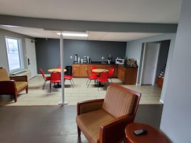 A dining area with red chairs and a wooden table, a kitchenette with a microwave, and a window with a view of the outside.