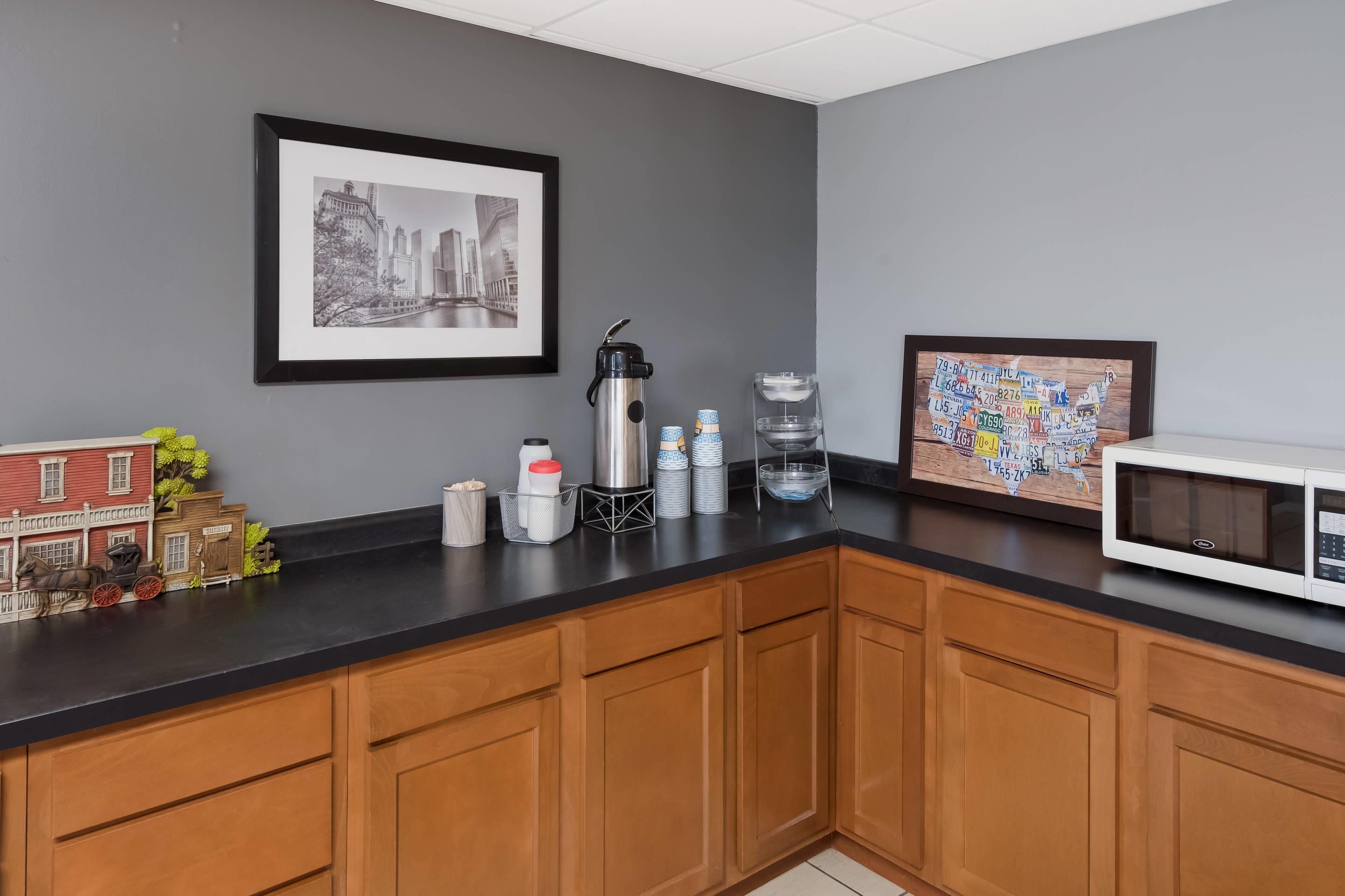 A kitchen with wooden cabinets, a black countertop, a coffee maker, a microwave, and a framed cityscape picture.