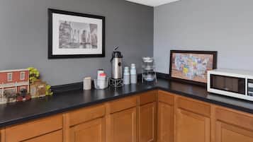A kitchen with wooden cabinets, a black countertop, a coffee maker, a microwave, and a framed cityscape picture.