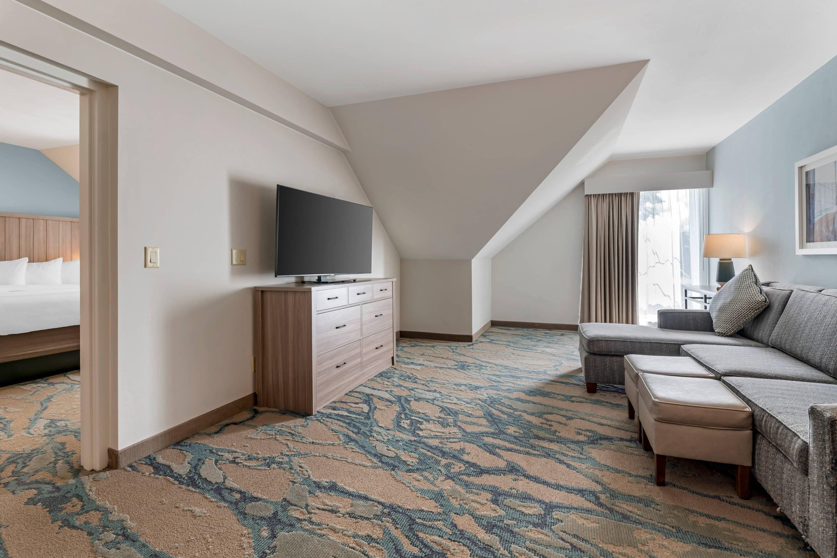 Una habitación de hotel con una cama grande, un sofá, un televisor sobre un aparador de madera y una alfombra estampada.