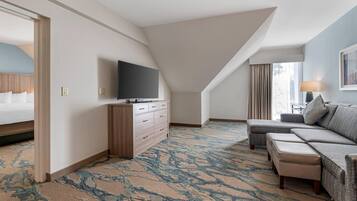 Una habitación de hotel con una cama grande, un sofá, un televisor sobre un aparador de madera y una alfombra estampada.
