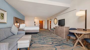 A hotel room with a bed, a sofa, a desk with a chair, a television, and a large mirror.
