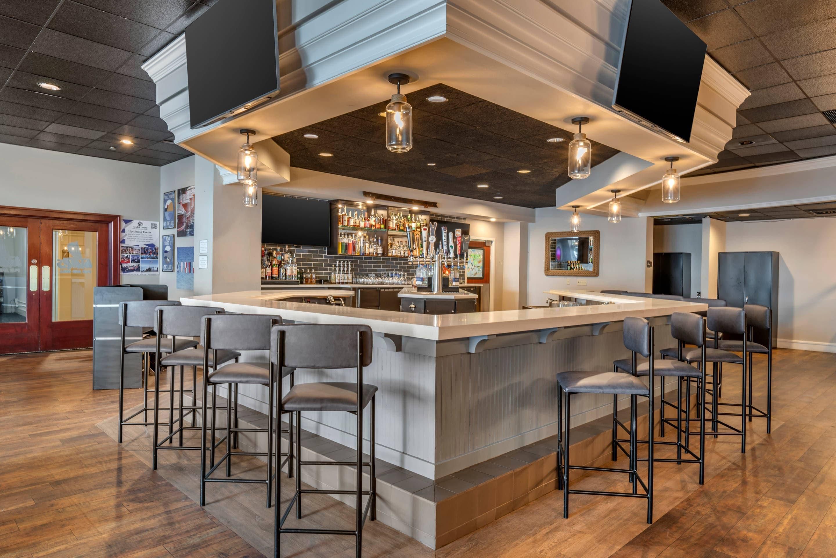 A bar area with a long counter, multiple stools, and a variety of bottles and glasses.