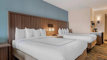 Habitación de hotel con dos camas, cabecero de madera, mesita de noche, lámpara y una pequeña mesa.