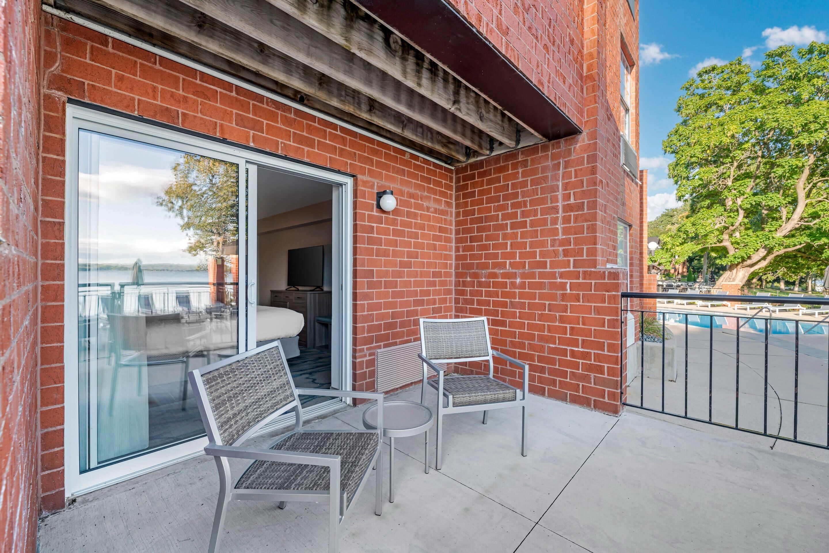 A balcony with a glass door leading to a room, two wicker chairs, and a small round table.