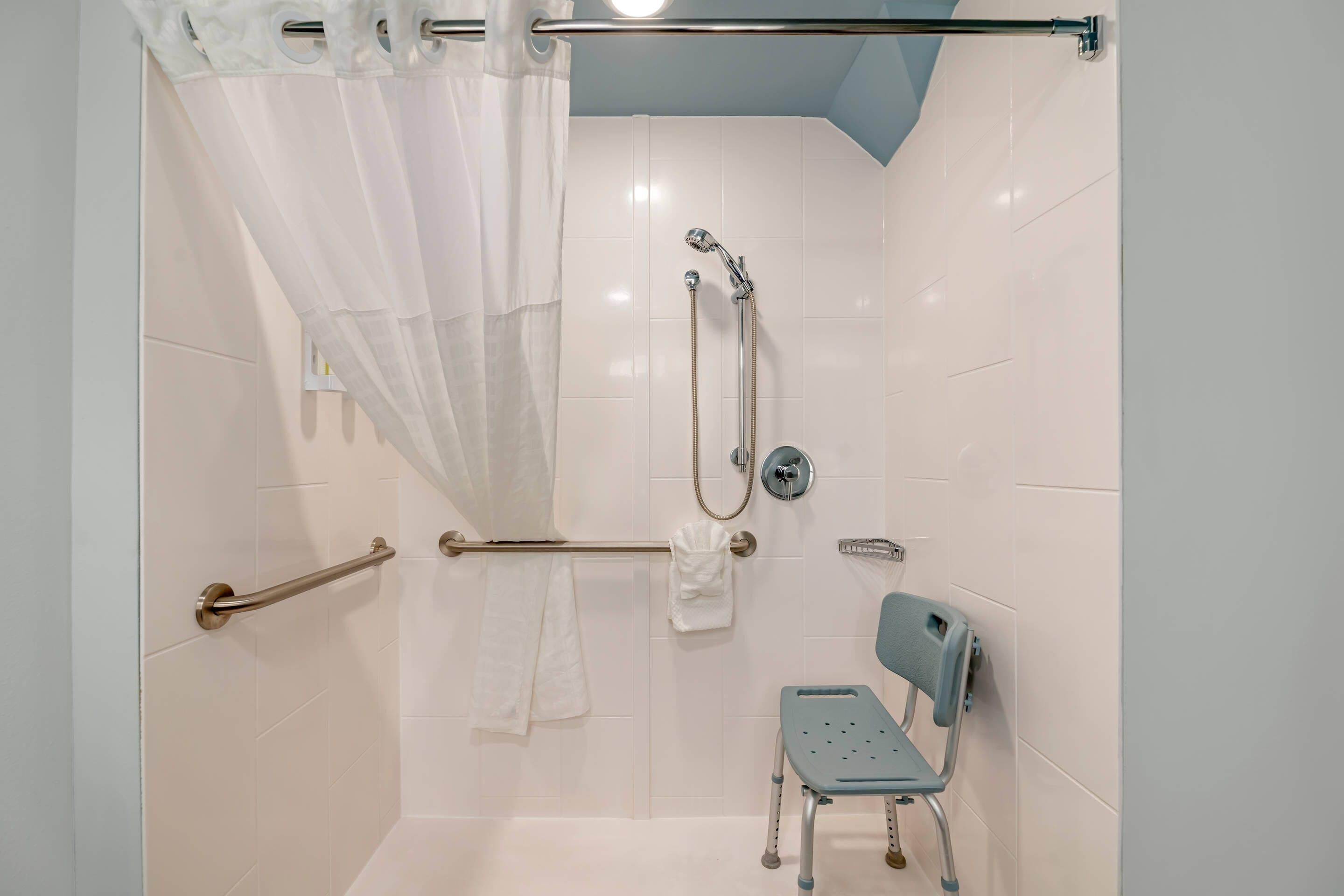 A shower area with a grab bar, a showerhead, a towel rack, and a wheelchair-accessible bench.