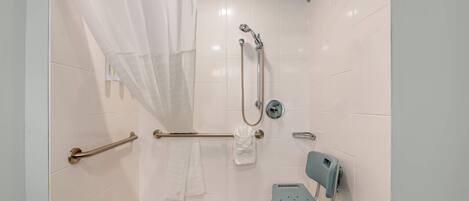 A shower area with a grab bar, a showerhead, a towel rack, and a wheelchair-accessible bench.