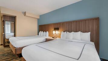 Habitación de hotel con dos camas, cabecero de madera, mesita de noche con lámpara y ventana con cortinas.