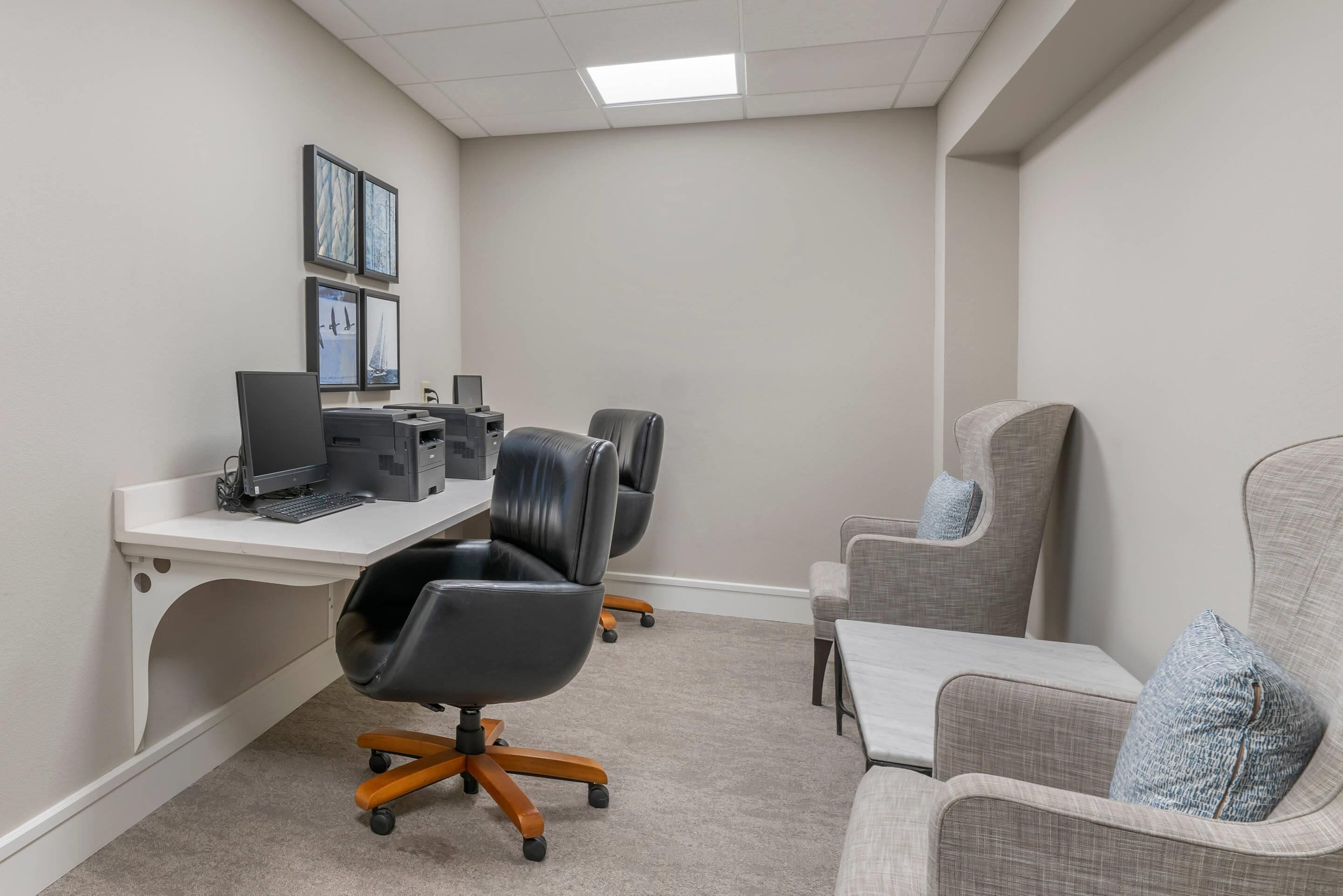 A conference room with a white desk, two black office chairs, a grey armchair, and a printer.
