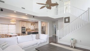 A spacious living area with a white sofa, a dark coffee table, and a staircase leading to an upper level.