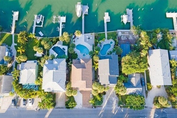 Vista aérea de una propiedad costera con múltiples piscinas, un puerto deportivo y abundante vegetación.