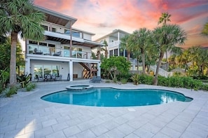 Una casa moderna de varios pisos con piscina, mobiliario exterior y palmeras.