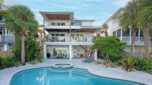 A modern two-story house with a swimming pool, outdoor furniture, and a wooden deck.