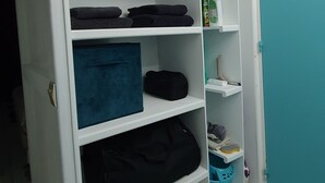 A white wardrobe with two doors, shelves with folded clothes, and a blue door to the right.