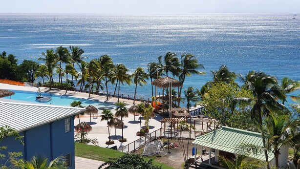 A resort with a swimming pool, palm trees, and a view of the ocean.