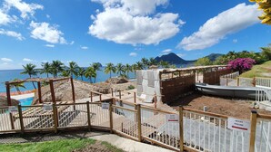 A beachside resort with a swimming pool, wooden deck, and a view of the ocean and mountains.