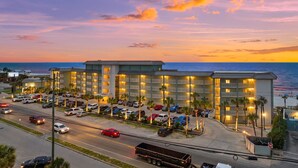 Un hotel con varios pisos, estacionamiento y vista al océano al atardecer.
