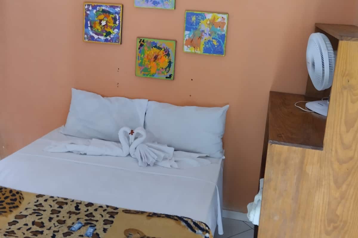 Een hotelkamer met een bed, een ventilator en drie schilderijen aan de muur.