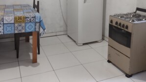 Een keuken met een betegelde vloer, een tafel met een tafelkleed met patroon, een koelkast en een gasfornuis.