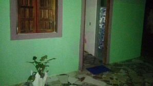 Een kamer met een groene wand, een houten deur, een raam met houten luik en een betegelde vloer.