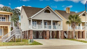 A two-story house with a balcony, brick foundation, and a clear blue sky.