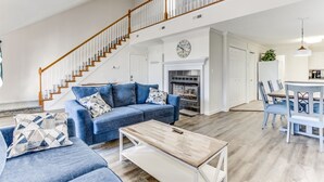 A spacious living room with a blue sofa set, a wooden coffee table, and a staircase with wooden railings.