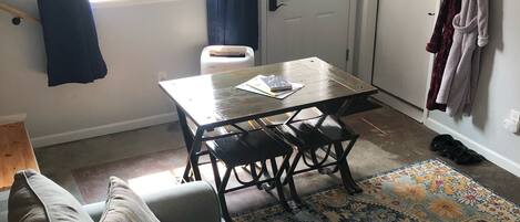 A living room with a sofa, a table with chairs, a patterned rug, and a door with curtains.