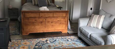 A bedroom with a wooden bed, a grey sofa, a patterned rug, and a wooden coffee table.