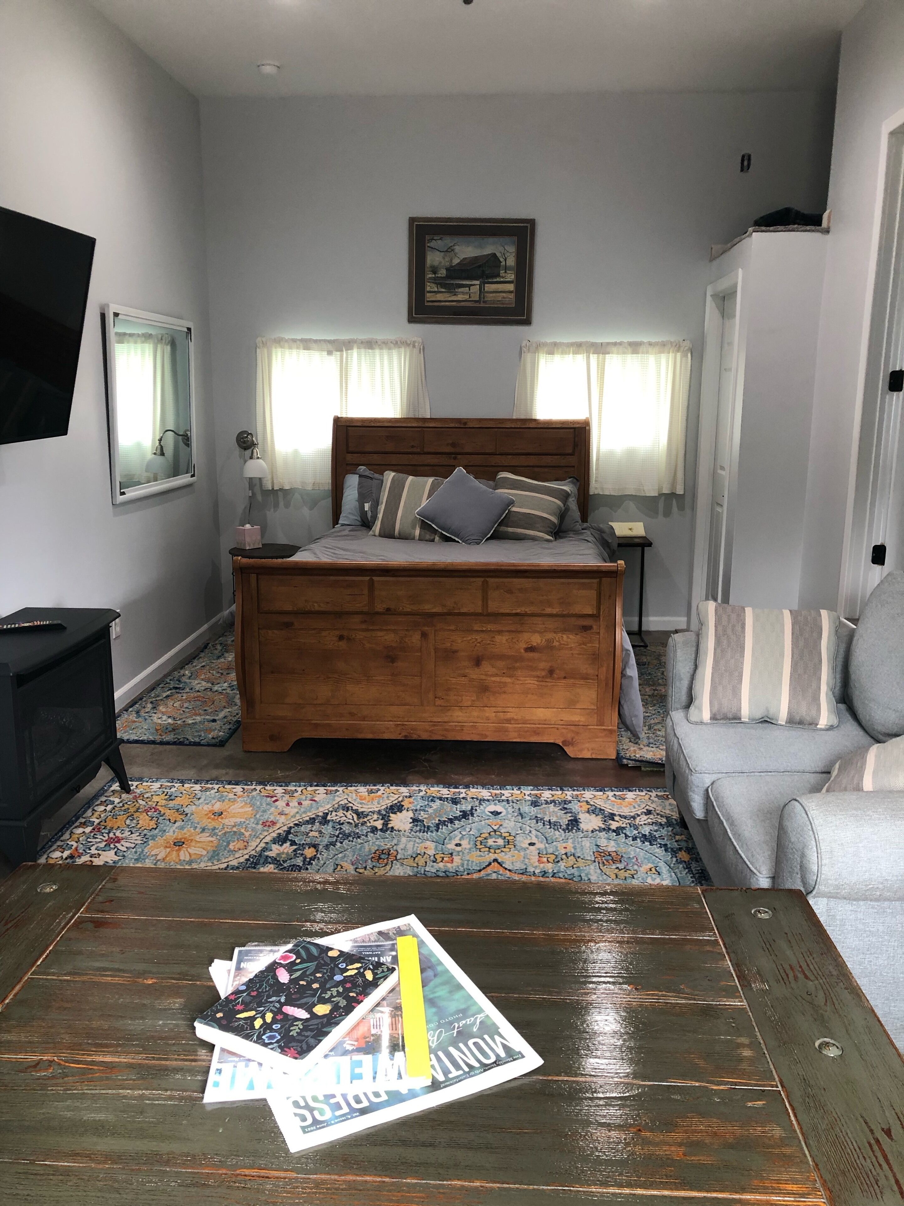 A bedroom with a wooden bed, a television on the wall, a sofa, and a patterned rug.