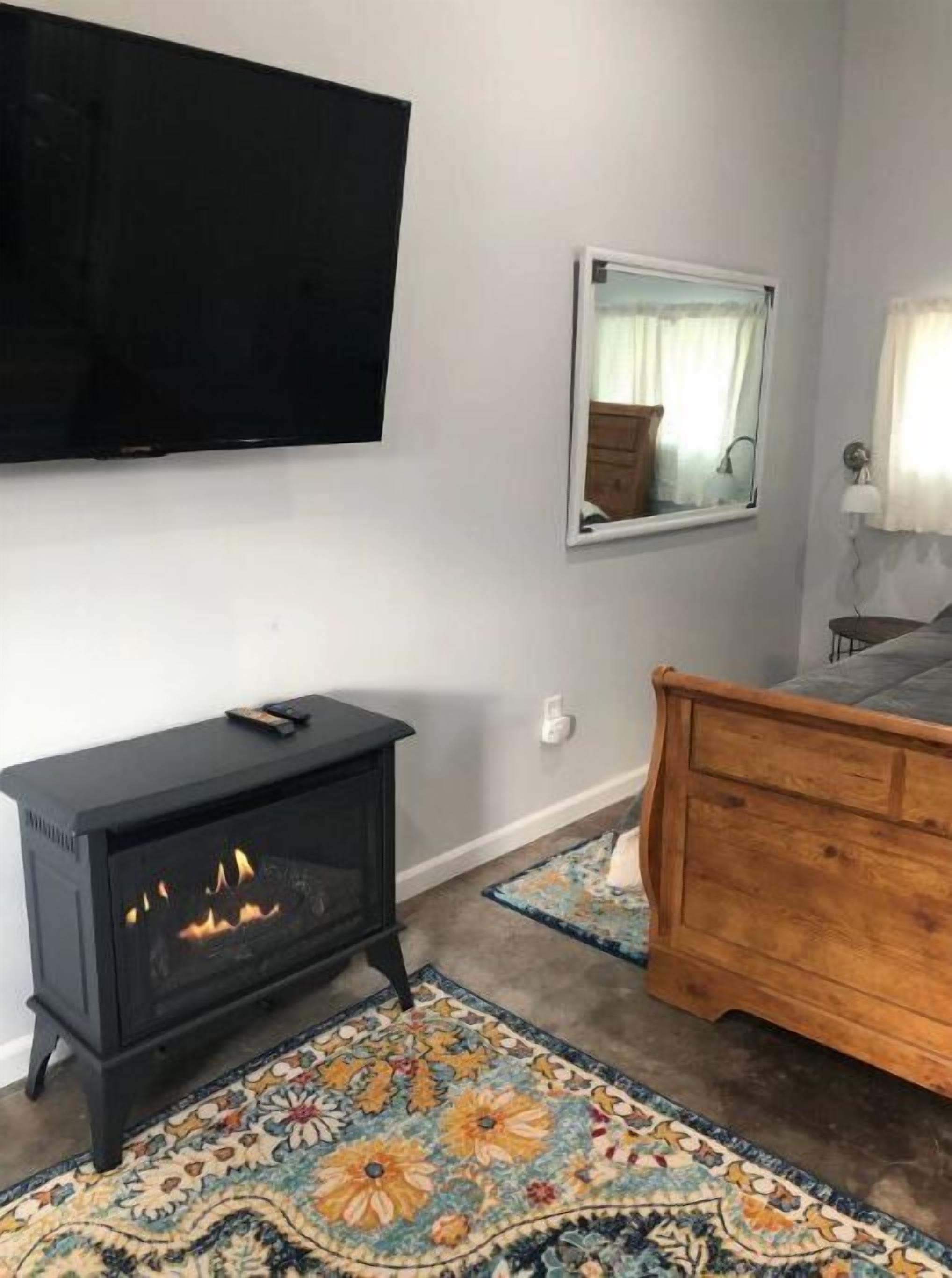 Une pièce avec une cheminée noire, une commode en bois, un miroir et un téléviseur fixé au mur.