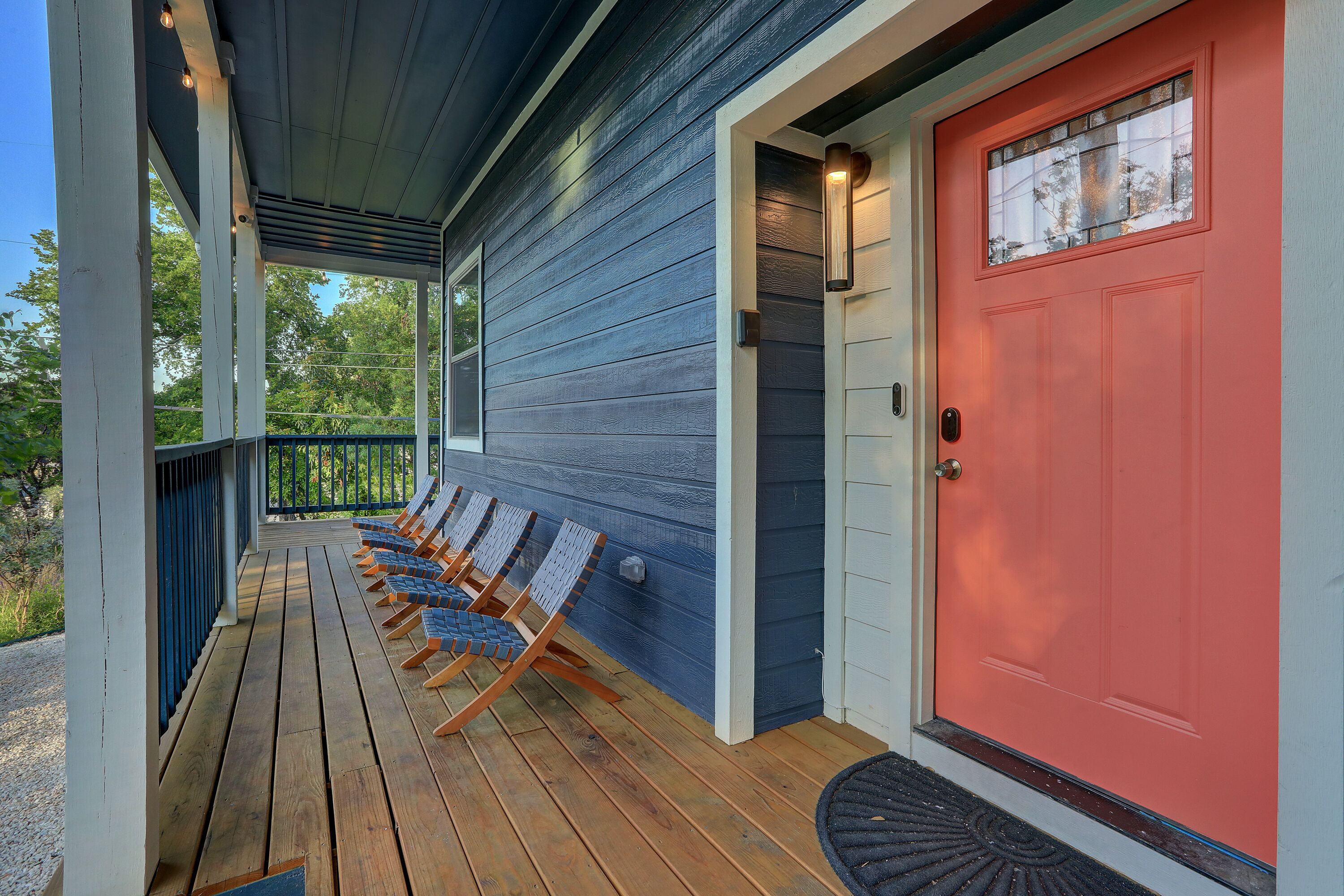 A porch with wooden flooring and metal railings, a red door, and a blue exterior wall.