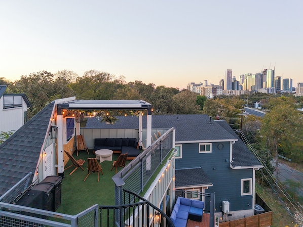 Une terrasse sur le toit avec un espace salon, une petite table et une pergola décorée de guirlandes lumineuses.